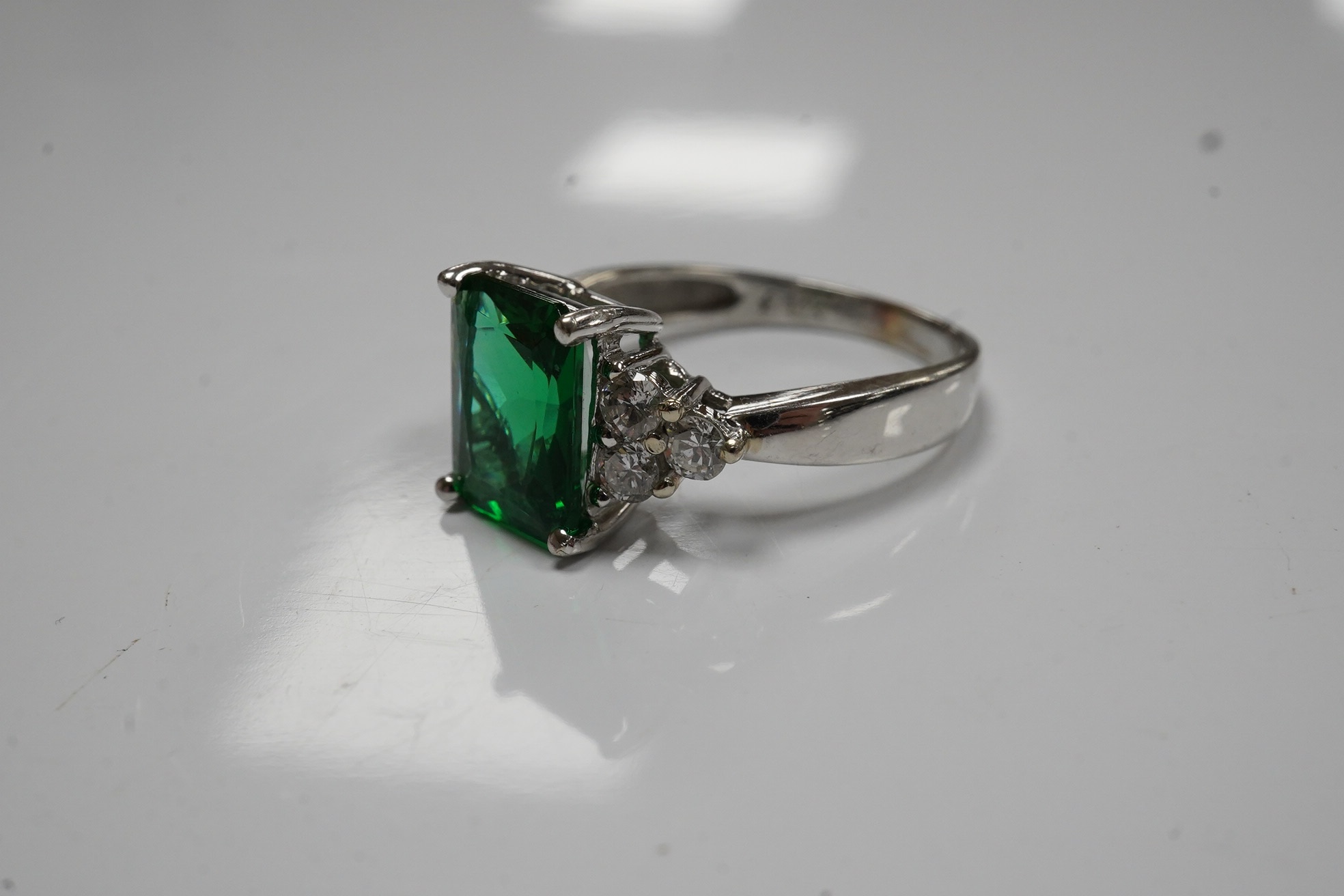 A modern 14k white metal and single stone green paste set dress ring, with six stone diamond set shoulders, size O, gross weight 3.6 grams. Condition - fair